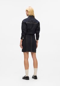 Dunkelblaue Denim-Jacke und Röcke-Set mit sichtbaren Nähten. Die Jacke hat einen Kragen und Knopfmanschetten; der Rock ist enganliegend mit geradem Schnitt.