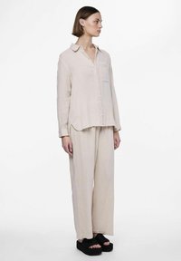 Camisa de botón beige claro con bolsillo, corte relajado, mangas largas y pantalones livianos a juego. Llevada con sandalias de plataforma negras.