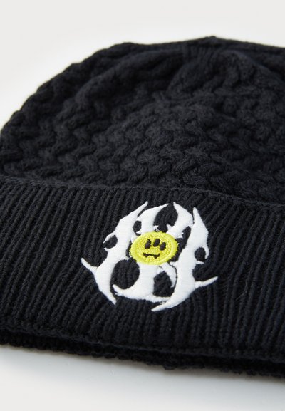 Căciulă tricotată neagră cu vârf texturat și margine ribbară. Prezintă un design brodat alb cu o față zâmbitoare galbenă în centru.
