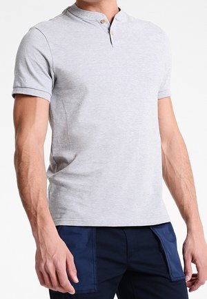 Homme portant un tee-shirt henley à manches courtes gris clair avec deux boutons et un pantalon bleu marine avec des poches avant.