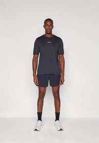 Tumehall sportlik lühikeste varrukatega T-särk, mida täiendab meresinine lühike pükste paar. Rindkerel väike logo. Valged tossud.