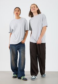 Gray cotton t-shirts, loose fit, worn with blue wide-leg jeans and dark pants. Sneakers feature multi-tone design with neon accents.