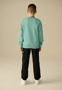 Mintgrøn sweatshirt med ribbede manchetter, parret med sorte sweatpants med en sidelomme. Hvide sneakers fuldender looket.