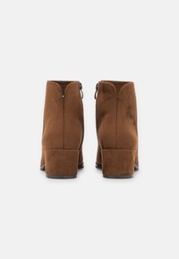 Stivali alla caviglia in suede marrone con tacco a blocco, chiusura con cerniera sul retro e texture liscia. Presenta una suola leggermente elevata.