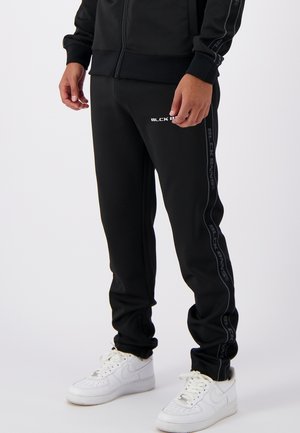 Black tracksuit pants with a slim fit, featuring white text logo and tonal side stripes, made of smooth, stretchy material.