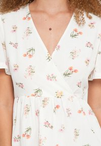 Φλοράλ φόρεμα τύπου wrap σε λευκό ύφασμα με ροζ και πορτοκαλί λουλούδια. Μανίκια κοντά, ντεκολτέ σε σχήμα V και λεπτομέρεια με σούρες στη μέση. Ελαφριά υφή.