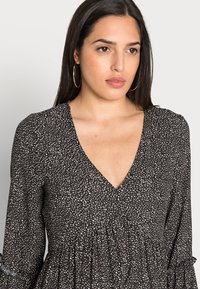 Vestido preto com padrão, decote em V, mangas longas e punhos franzidos. O tecido apresenta um padrão abstrato leve e uma cintura franzida.