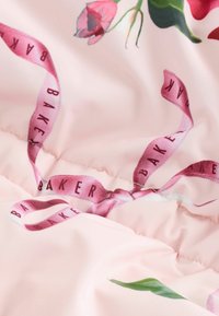 Lyse pink stof med blomsterprint og et lyserødt bånd med teksten "BAKER", der fremhæver et legende og elegant design.