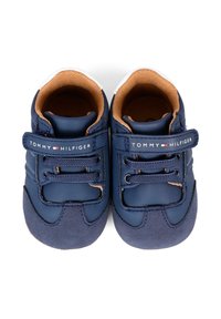 Un paio di scarpe da ginnastica per neonati blu navy con rifinitura interna marrone, lacci blu navy e un logo Tommy Hilfiger sulla cinghia.