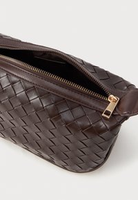 Pochete de couro trançado castanho com detalhes em zíper dourado, apresentando um padrão texturizado e bordas arredondadas. O zíper aberto revela o interior.