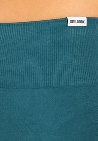 Türkisfarbener dehnbarer Stoffbund mit gerippter Textur und einem kleinen weißen Etikett mit der Aufschrift "SMILODOX." Glatte, einfarbige Oberfläche ohne zusätzliche Muster.