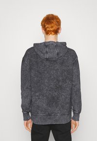 Felpa con cappuccio grigia scura realizzata in un tessuto morbido e texturizzato. Presenta un cappuccio con coulisse e polsini e orlo a coste. Senza loghi o motivi visibili.