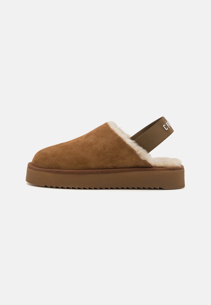 Brune semskede slip-on tøfler med fòring i pels, flad såle og en snørestrop med et kontrasterende logo-detalje.