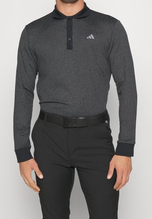 Homme portant un polo à manches longues gris foncé avec col noir et pantalon noir, équipé d'une ceinture noire avec une boucle à logo.