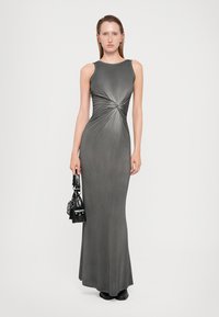 Abito maxi grigio senza maniche con dettaglio a spirale in vita, texture liscia e silhouette aderente. Il modello tiene una piccola borsa nera.