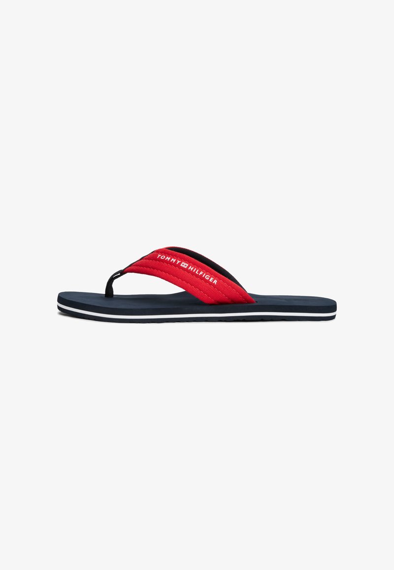 Röd och svart flip-flop med texturerade remmar och en vadderad marinblå sula; har en vit logotyp och en randig kant i botten.