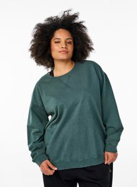 Felpa verde scuro, realizzata in tessuto morbido, con scollatura rotonda, spalle ribassate e vestibilità rilassata. Polsini e orlo a costine.
