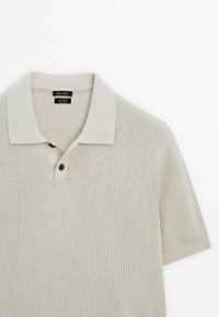 Vaaleanbeige neulottu poolopaita, jossa on litteä kaulus, kolmen napin lista ja lyhyet hihat resorikärkineen.