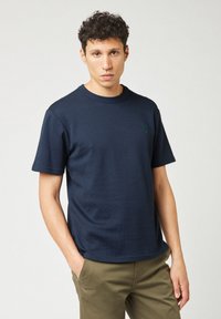 T-shirt blu navy a maniche corte realizzata in tessuto testurizzato, con scollatura rotonda e un piccolo logo verde sul petto.