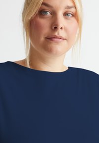 Marineblaues Oberteil mit einem breiten, geraden Ausschnitt, aus glattem Stoff gefertigt. Es hat eine lockere Passform, eine sichtbare Schulterlinie und ein schlichtes Design.