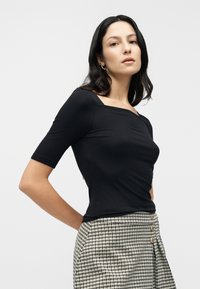 Μαύρο εφαρμοστό τοπ με τετράγωνο ντεκολτέ και κοντά μανίκια, σε συνδυασμό με ψηλόμεσα παντελόνια με μοτίβο κυνόδοντα και κουμπιά.