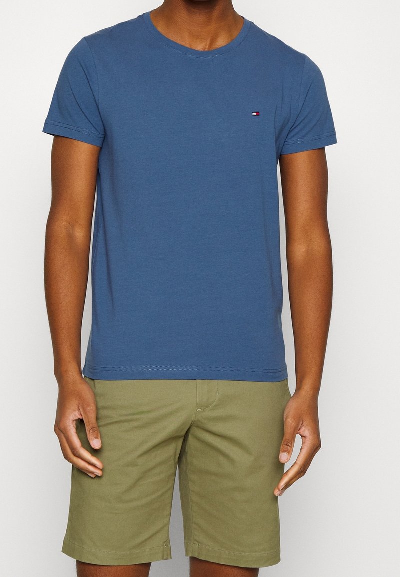 Blauwe katoenen T-shirt met korte mouwen, ronde hals en een klein geborduurd logo op de borst. Gepaard met kaki shorts.