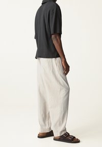 Polo negro de manga corta con tejido texturizado, combinado con pantalones sueltos de color claro con rayas y sandalias marrones de dos hebillas.