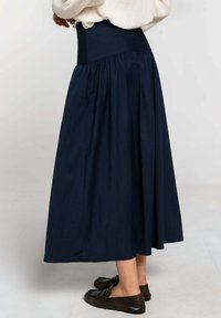 Falda larga azul marino hecha de tela suave, con una cintura alta y diseño plisado, combinada con zapatos planos oscuros.