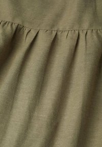 Khaki-Stoff mit einer weichen Textur, der oben mit gerafften Details versehen ist, was einen subtilen Wellen Effekt erzeugt.