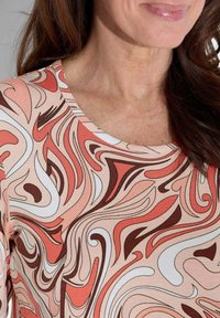 Langsleeve top van zachte stof, met een draaiend patroon van koraal, wit en bruin met een ronde halslijn.