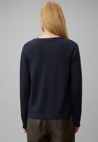 Mörkblå stickad tröja med avspänt snitt, texturerad tyg, ribbade manschetter och rund halsringning; bärs med mörkbruna byxor.