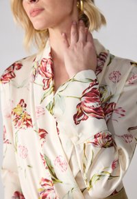 Floral blouse in cream fabric featuring large red and pink tulip patterns. Includes a double-breasted design with soft cuffs and button details.
