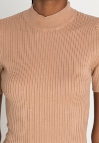 Top en maille côtelée beige clair avec un col rond haut et des manches courtes, présentant une texture lisse et une coupe ajustée.