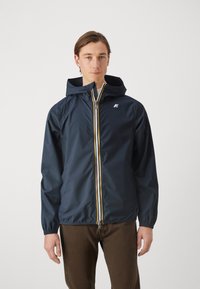 Marineblauwe waterdichte jas met een capuchon, voorrits met gele accenten en elastische manchetten. Klein logo op de borst. Tailored fit.