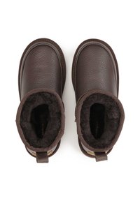 Botas de tobillo de cuero marrón con suave forro de piel de oveja negra, punta redonda y acentos cosidos. Incluyen una lengüeta en el talón para facilitar su uso.