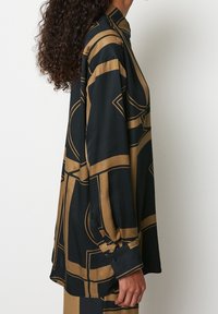 Sort og guldmønstret skjorte med afslappet pasform, lange ærmer, knaplukning ved manchetterne og høj halsudskæring. Glat, let stof med geometriske mønstre.