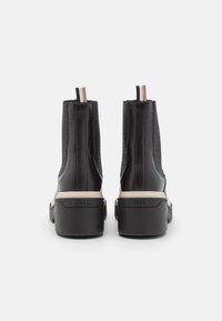 Botas de tobillo de cuero negro con secciones de malla, suela gruesa y acentos en beige. Presentan un logo en el talón y aletas para facilitar su uso.