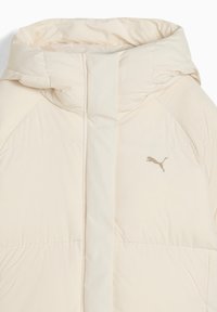Giacca puffer in beige chiaro, con colletto alto, texture liscia e un sottile logo dorato sul petto, con dettagli di cucitura.