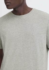 Camiseta de manga corta gris claro, hecha de una suave mezcla de algodón. Presenta un sutil logo bordado en el pecho. Cuello redondo, ajuste relajado.