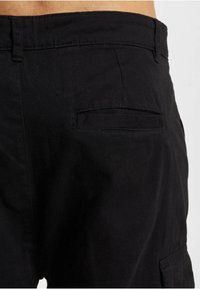 Black cotton pants with a smooth texture, featuring a back pocket and a fitted waistband. The design is simple with no visible hardware.
