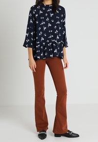 Haut péplum floral bleu marine avec manches cloche, associé à un pantalon évasé marron et des mocassins noirs ornés d'un accent chaîne.