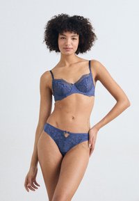 Lace bra and matching thong in deep blue. Bra features underwire, delicate lace detailing, and chain accents; thong includes a small keyhole cutout.