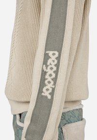 Μπεζ πλεκτό πουλόβερ με γκρι κατακόρυφη ρίγα που διαθέτει ανάγλυφο κείμενο στο μανίκι. Υφασμάτινη επιφάνεια με ριμπ μανσέτες.