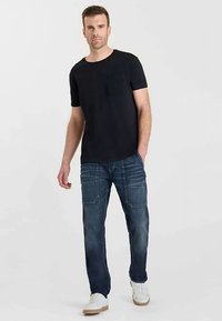 Svart t-shirt med korta ärmar och en bröstficka, kombinerad med mörkblå denimjeans med synliga sömmar och framfickor. Vita sneakers.