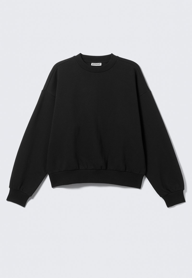 Crna majica s okruglim izrezom, ležernog kroja, spuštenih ramena i rebrastim manšetama i rubom, izrađena od mekanog, teksturiranog tkanja. Bez vidljivih detalja.