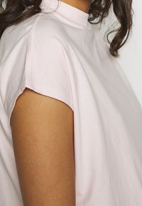 Ljust rosa, kortärmad topp med hög krage, tillverkad av mjukt bomullstyg. Har råa kanter på ärmsluten och en minimalistisk design.