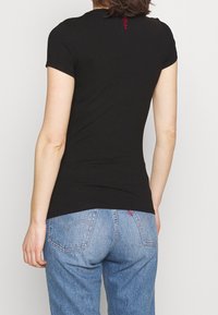 Camiseta negra de manga corta ajustada con escote redondeado y un pequeño logo rojo en la parte posterior, combinada con unos jeans de mezclilla azul claro.