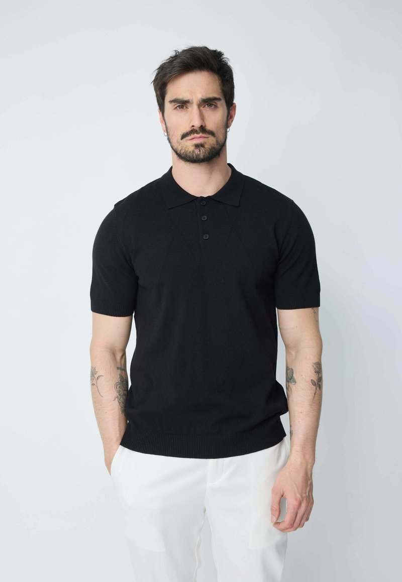 Polo noir à manches courtes en tissu tricoté avec un col à trois boutons et des poignets côtelés, associé à un pantalon clair.