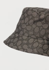 Μαύρο καπέλο μπ bucket με υφαντή υφή που διαθέτει οβάλ σχέδιο. Διαρθρωμένο γείσο και διακριτική λεπτομέρεια λογότυπου στο πλάι.