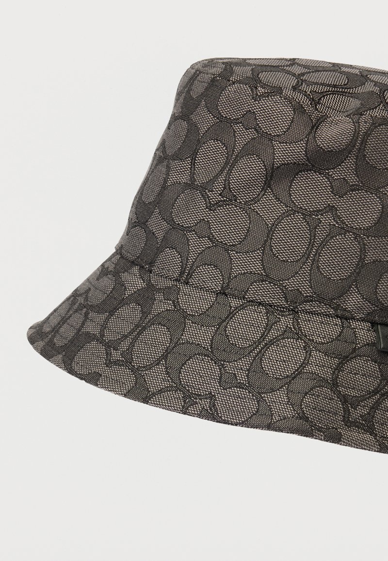 Chapeau seau noir avec une texture tissée présentant un motif ovale. Large bord structuré et détail de logo subtil sur le côté.